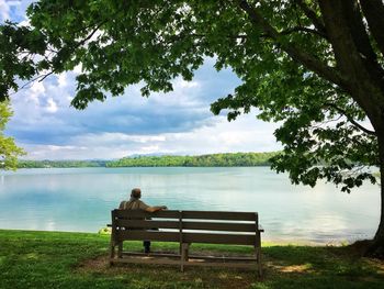 Rear view of man sitting by lake against sky