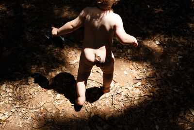 Low section of naked baby boy walking on field