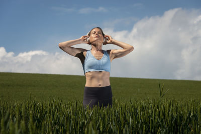 Sporty, fit woman standing in a green field wearing a pair of headphones listening to music.