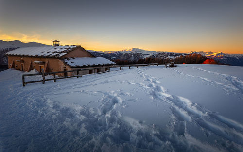 Snow covered houses and buildings against sky during sunset