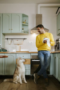 Mid adult man drying hands while looking at siberian husky dog in kitchen