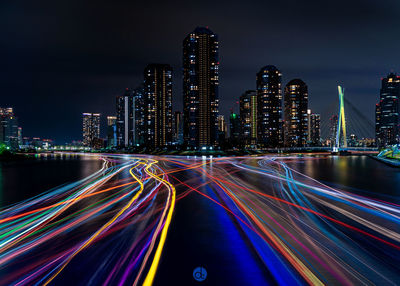 Light trails on road by illuminated buildings at night