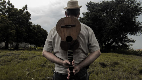 Rear view of man holding ukulele while standing on grassy field