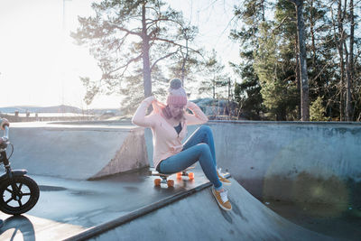 Woman sat on a skateboard in a skatepark smiling in the sun