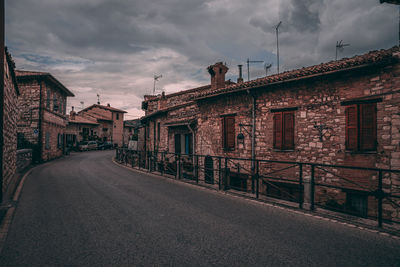 Empty road by buildings in city against sky