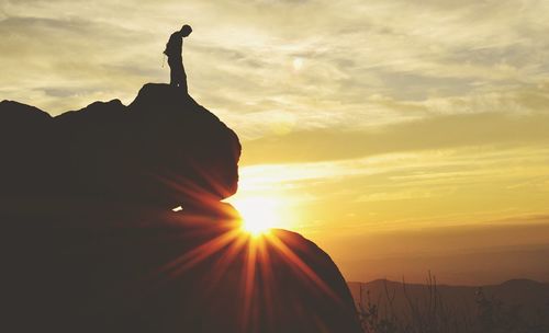 Silhouette man standing on cliff against shining sun