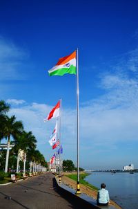 Low angle view of various flags by mekong river against cloudy blue sky