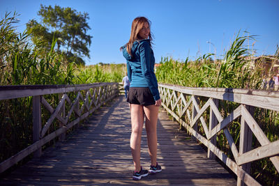 Rear view of woman standing on footpath by footbridge