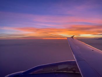 Airplane wing against sky during sunset