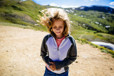 Girl with tousled hair standing on field against mountain