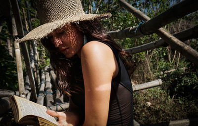 Midsection of young woman reading book by tree