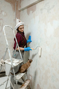 Girl painter paints the walls with a roller.  her cat is next to her.  funny