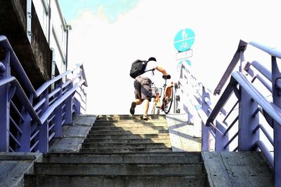 Low angle view of man with bicycle walking on staircase against sky at subway