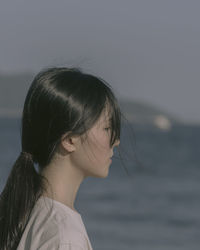 Side view of thoughtful woman standing at beach against sky