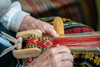 Cropped hands of woman weaving thread at home