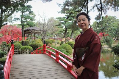 Portrait of smiling japanese woman in kimono standing on footbridge