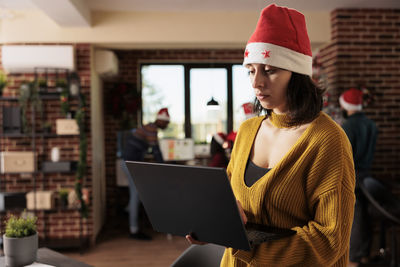 Young woman using laptop while standing in office