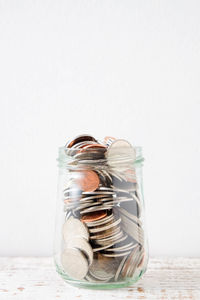 Close-up of coins in jar on table against wall