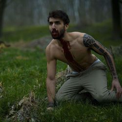 Bleeding shirtless man kneeling on grassy field