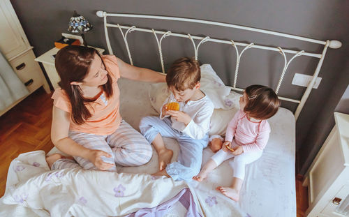 Cheerful mother playing with son and daughter while eating on bed at home
