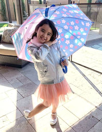 Portrait of young girl with umbrella walking on street
