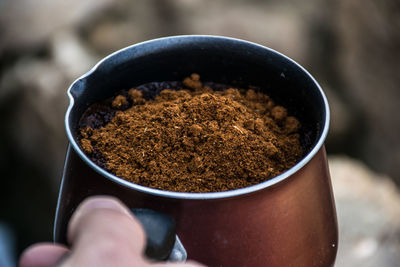 Close-up of hand holding ground coffee in container