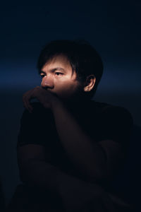 Sad man sitting in darkroom against blue wall