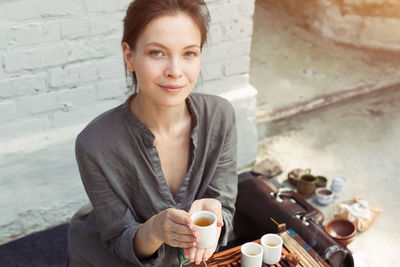 Portrait of woman holding tea cup against brick wall