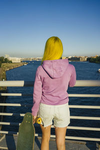 Rear view of woman standing by railing against sea