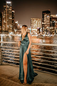 Full length of woman standing by modern buildings in city at night