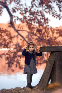 Autumn vintage portrait of a cute girl in a boater hat on a background of red foliage and a pond