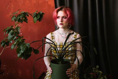 Young woman holding potted plant while looking away