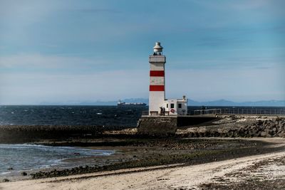 Lighthouse on beach against sky