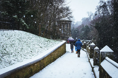 Rear view of people walking on footpath during snowfall