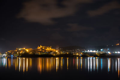 Illuminated buildings by sea against sky at night