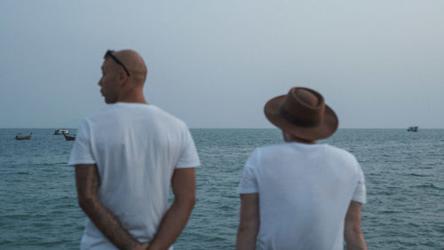 Rear view of men standing by sea against clear sky