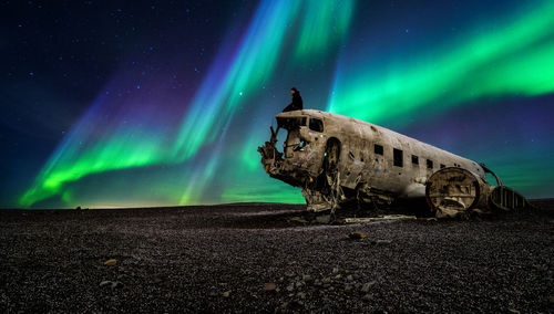 Abandoned airplane on land against aurora borealis at night