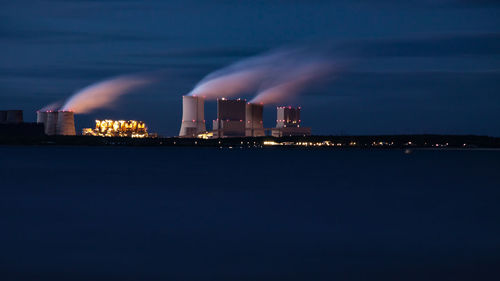 Illuminated city by sea against sky at night