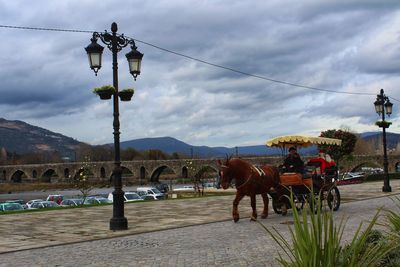 People riding horse cart on mountain against sky