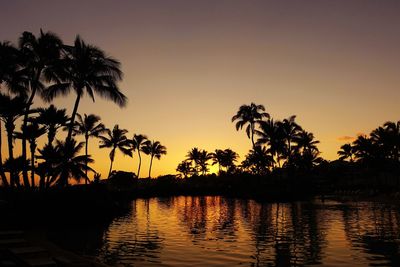 Silhouette palm trees by lake against sky during sunset