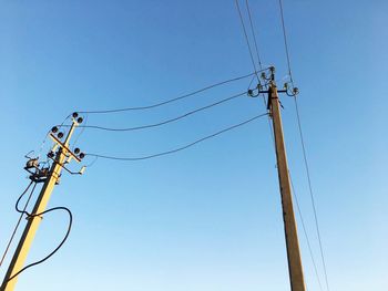 Low angle view of electricity pylons against clear blue sky