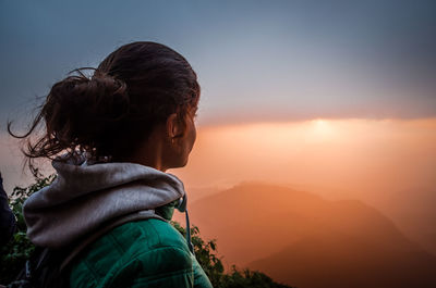 Woman looking at mountains against sky during foggy sunrise