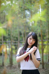 Portrait of beautiful young woman standing against trees