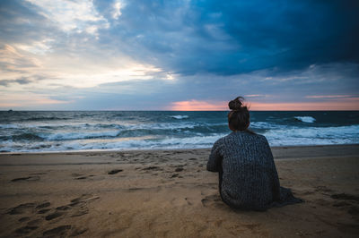 Rear view of woman looking at sea against sunrise sky on the beach