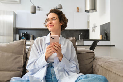 Young woman using phone while sitting on bed at home