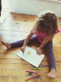 High angle view of girl drawing while sitting on hardwood floor