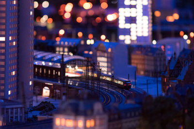 Tilt-shift image of train on railroad tracks in illuminated city