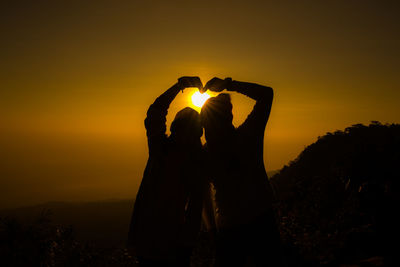 Silhouette of couple making heart shape against sky during sunset