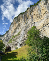 Low angle view of rocky mountains and waterfall against sky