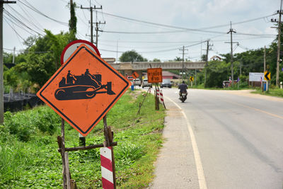 Road sign by street against sky in city